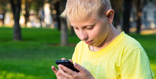 Boy Using Mobile Phone in a Green Park