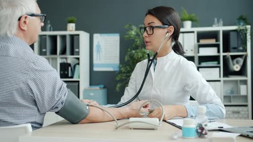 Female Doctor Checking Blood Pressure Examining Elderly Man Patient in Hospital