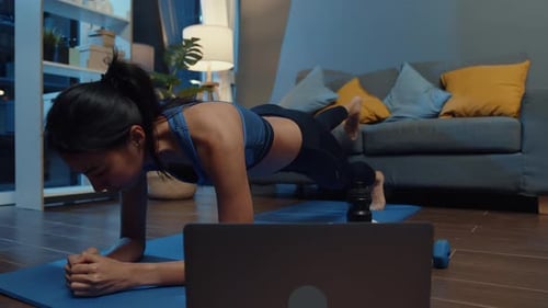 Mujer asiática en ropa deportiva haciendo ejercicio y usando el teléfono para ver un vídeo tutorial de yoga.