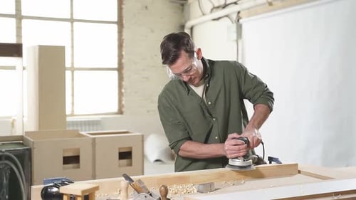 Man Sanding Wood with Electric Sander in Workshop