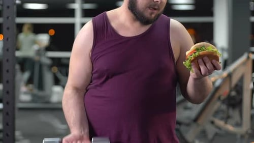 Man Lifts Weights While Holding a Burger at Gym