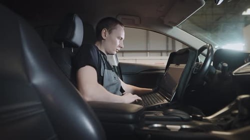 Ein Mann ist ein Mechaniker, der im Auto sitzt und eine Computerdiagnose des Motors und der Systeme durchführt