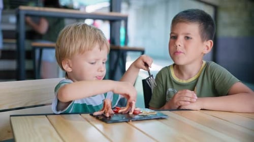 Brothers Eating Sausages at a Restaurant Table