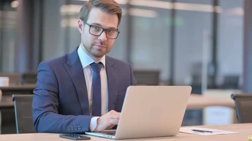 Confident Businessman Working at Laptop in Office