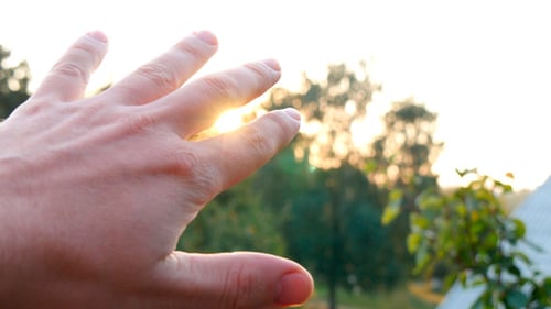 Mann blickt durch Finger zur Sonne