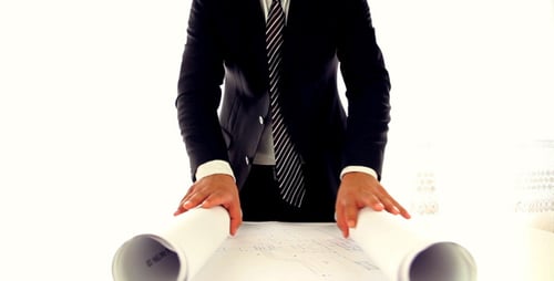 Professional Architect Unrolls Blueprints in Workplace