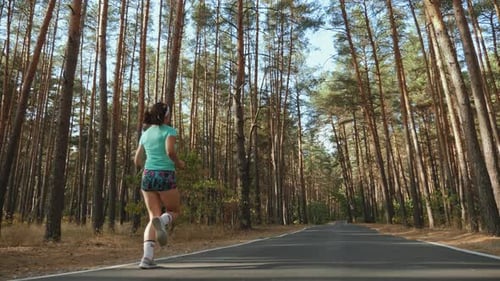 Athletic Girl Runs Along the Road in a Pine Forest