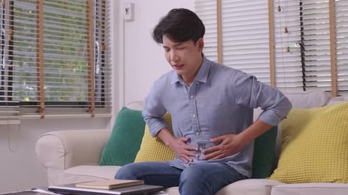 Hand eines asiatischen Mannes, der den Magen hält und unter Schmerzen und Durchfall leidet