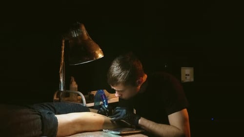 Tattoo Artist Inking Leg Tattoo in Dark Studio