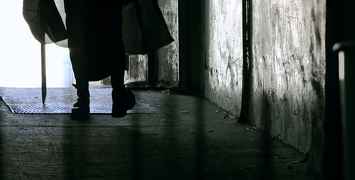 Person Walking with Stick in Dark Urban Corridor