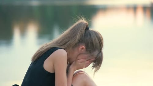 Sad Young Woman Crying By Pond at Sunset