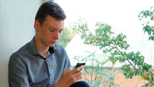 Young Man Using Smartphone by Window