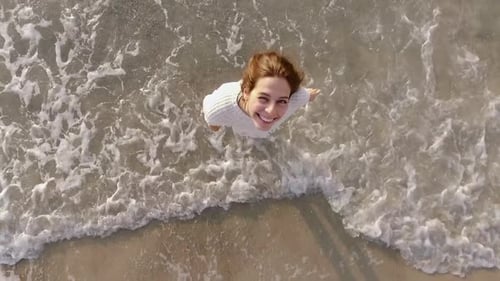 Smiling Woman Stands in Ocean Waves, Birds Eye View