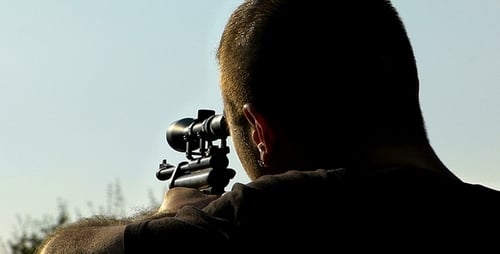 Man Aims Rifle Outside on Sunny Day