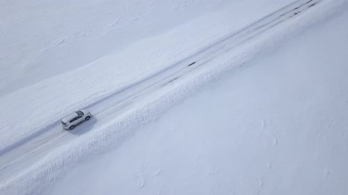 Luftaufnahme eines Autos, das durch die Winterwaldstraße zwischen den schneebedeckten Feldern fährt
