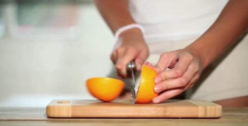 Woman Slices Orange on Cutting Board at Home