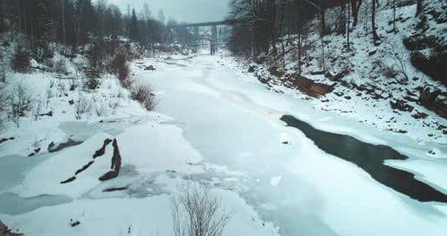Der gefrorene Fluss im Winterwald ist mit verschneiter Luftaufnahme bedeckt