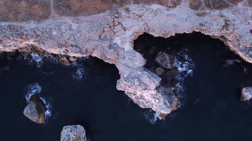 Top down aerial view of waves splash against rocky seashore, background. Flight over high cliffs of