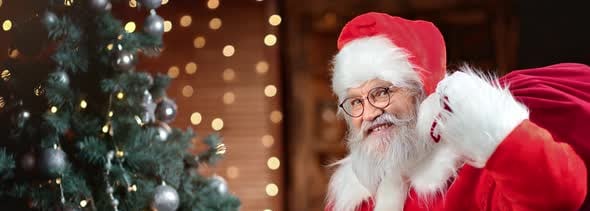 Funny Man in Santa Claus Costume Posing with Sack of Gifts at Christmas Tree