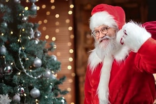 Funny Man in Santa Claus Costume Posing with Sack of Gifts at Christmas Tree