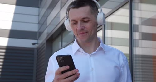 Man in headphones uses smartphone near modern building