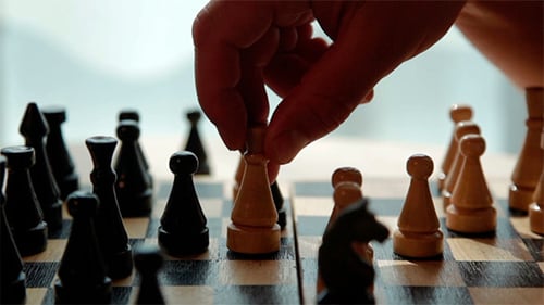 Hand Moving Pawn on Chessboard in Room