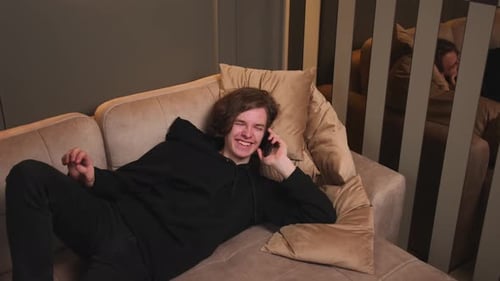 Smiling Young Adult Chatting on Phone on Sofa