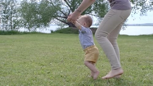 Baby Taking First Steps with Mother in Park