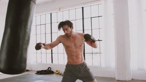 Muscular Man Punches Heavy Bag in Bright Gym