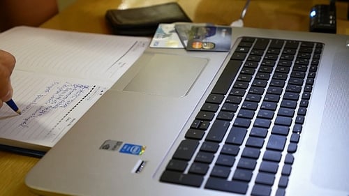 Person Writing in Notebook Next to Laptop