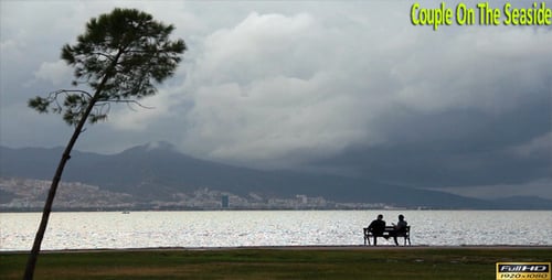 People Sit On Park Bench By The Ocean