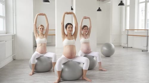Gruppe von Frauen in Sportbekleidung, die auf einem Fitnessschwert sitzend Übungen für Schwangere machen