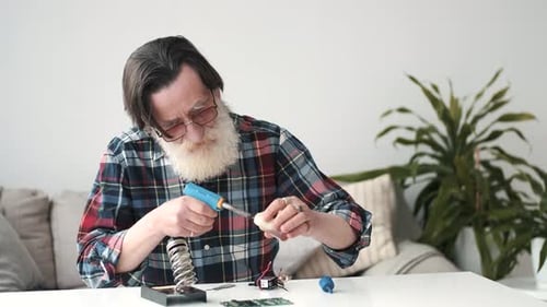 Man Soldering Electronic Components at Table Indoors
