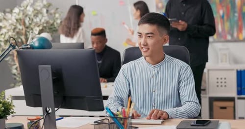 A Man of AsianKorean Beauty is Sitting an Office Computer Using a Web Browser Working in Front of a