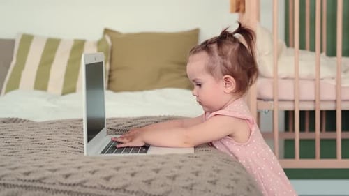 Cute Child Interacts With Laptop on Bed