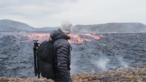 Photographer Walking With Rucksack Close To Flowing Lava