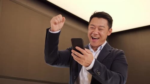 Portrait of Happy Asian Businessman Enjoy Success on Mobile Phone at Office