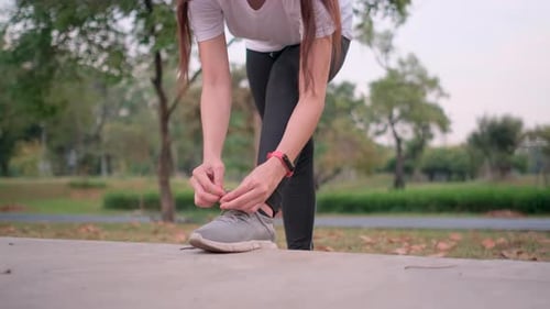 Portrait of Asian sport woman sit and tight her shoelaces during exercise in green park