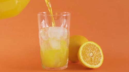 Refreshing Orange Juice Pouring into Glass with Ice