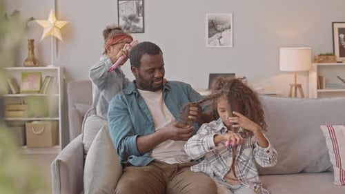 Man Sits as Two Girls Brush His Hair