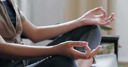 Femme portant des vêtements décontractés en jean assise sur un canapé dans une pièce en position de lotus avec jambes croisées