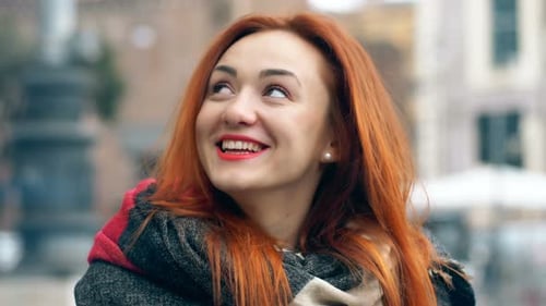 Happy beautiful red haired woman in the street smiling at camera