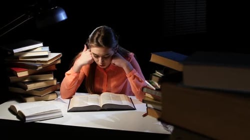 Girl Leafing Through a Book and Falling Asleep at the Table. Black Background
