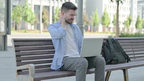 Man on Laptop on Park Bench Massages Neck