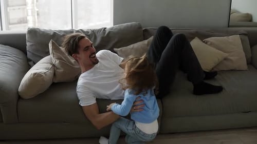 Father Plays with Joyful Child on Couch at Home