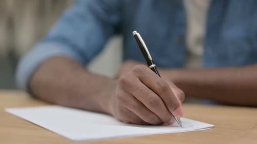 Nahaufnahme der Hände eines afrikanischen Mannes, der auf Papier schreibt