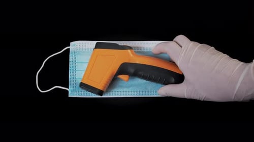 Doctor Puts a Contactless Infrared Thermometer on a Medical Mask. The Doctor Holds a Thermometer in