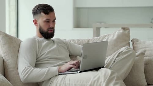 Man Works on Laptop While Relaxing on Sofa