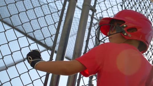 Child in Baseball Helmet Standing by Fence