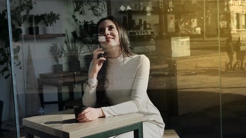 Pretty Young Woman with a Smartphone in Cafe with a Cup of Coffee Smiling